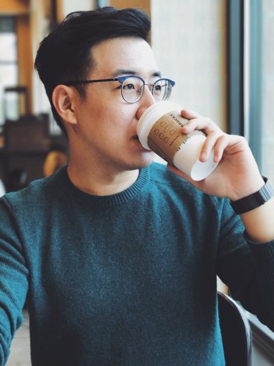 man with glasses and a sweater drinking coffee